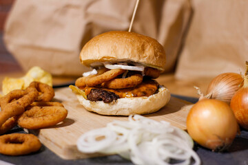 Burger w artystycznej kompozycji z frytkami i batatami oraz cebulą pieczarkami. Burgerownia - zdjęcie świeżego, apetycznego burgera
