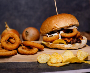 Burger w artystycznej kompozycji z frytkami i batatami oraz cebulą pieczarkami. Burgerownia - zdjęcie świeżego, apetycznego burgera