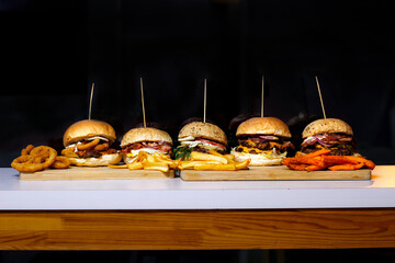 Burger w artystycznej kompozycji z frytkami i batatami oraz cebulą pieczarkami. Burgerownia - zdjęcie świeżego, apetycznego burgera
