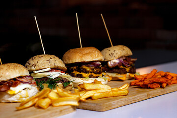 Burger w artystycznej kompozycji z frytkami i batatami oraz cebulą pieczarkami. Burgerownia - zdjęcie świeżego, apetycznego burgera