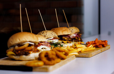 Burger w artystycznej kompozycji z frytkami i batatami oraz cebulą pieczarkami. Burgerownia - zdjęcie świeżego, apetycznego burgera