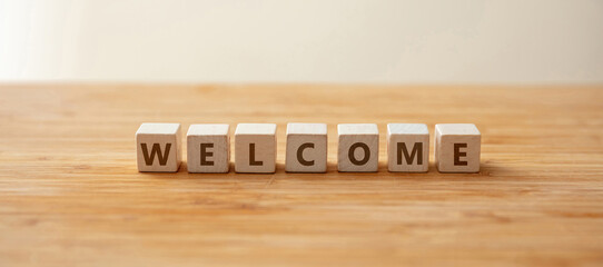 Welcome text on wooden cube on wooden table background, hospitality message. Overhead view. Banner