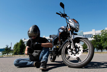 a motorcyclist in a helmet sits on the road next to a motorcycle and looks at the phone