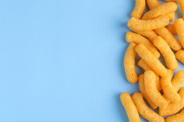 Heap of tasty cheesy corn puffs on light blue background, flat lay. Space for text