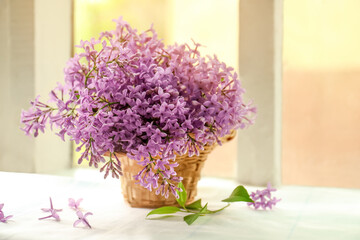 Beautiful lilac flowers in wicker basket on window sill indoors