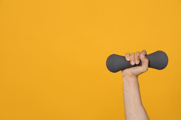 Man holding dumbbell on orange background, closeup. Space for text