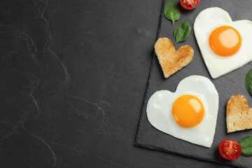 Heart shaped fried eggs and toasts on black table, top view. Space for text