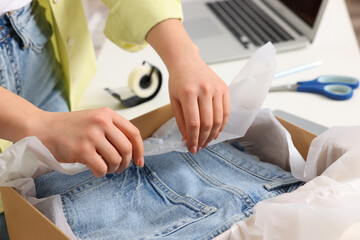 Seller packing jeans into cardboard box at workplace, closeup