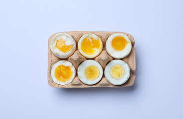 Boiled chicken eggs of different readiness stages in carton on white background, top view