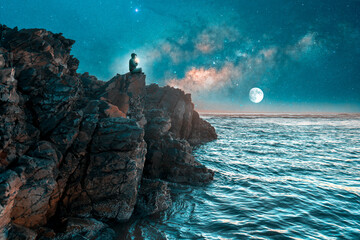 silhouette of a person meditating on cliff at night with milky way over the sea