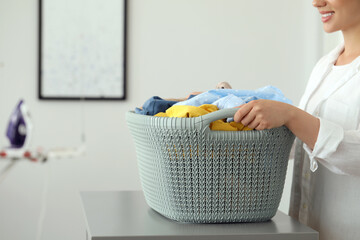 Woman with basket full of clean laundry at grey table indoors, closeup