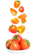 Sweet ripe persimmons falling into bowl on white background