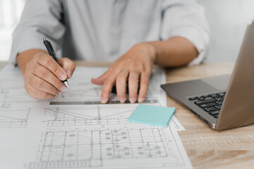 Fototapeta premium Engineering work concept: Close up hand a use pencil and steel ruler mark CAD drawing and calculator in Calculating document and laptop on the wood table in office
