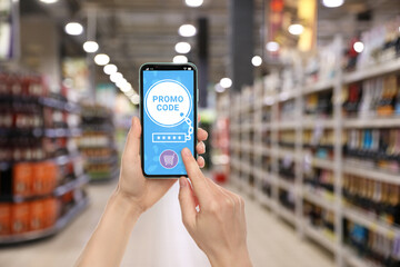 Woman holding smartphone with activated promo code in supermarket, closeup