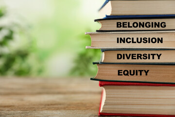 Stack of hardcover books with words Belonging, Diversity, Equity, Inclusion on wooden outdoors....