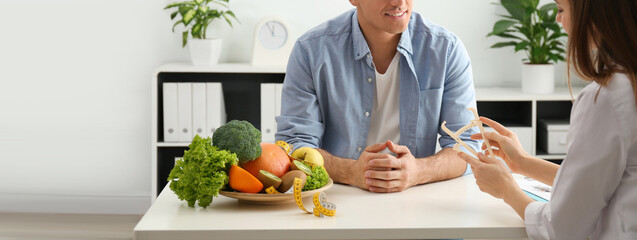 Young nutritionist consulting patient at table in clinic, closeup. Banner design