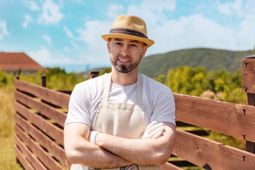 Portrait of a smiling handsome Caucasian bearded man in a straw hat, gloves and apron posing...