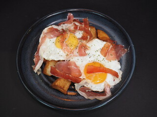 Organic Eggs with potatoes and Ham served in a dish isolated on dark background top view