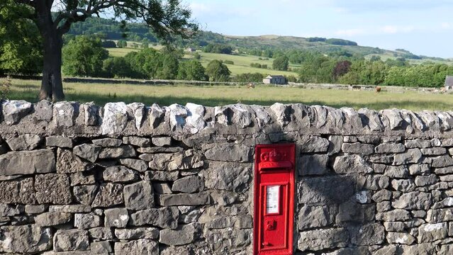 Tilt up shot showing red letter box in the stone fence in rural England in summer.