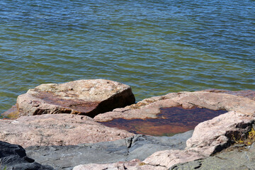 Rocks and stones meeting calm water surface of the Baltic Sea seashore in Helsinki, Finland. Sunny summer day asking you to travel, explore and swim the blue waters! Scenic coastline view. Color image