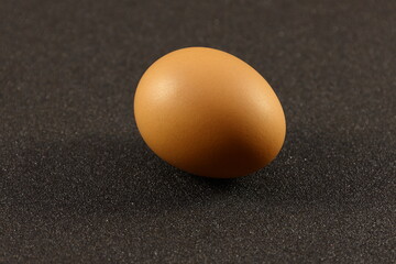 A light brown chicken egg on top of black sanding paper.