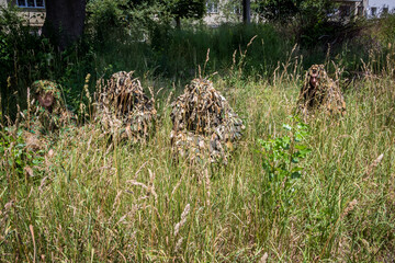 a girl and volunteers sit in camouflage robes - kikimors in the grass made for the front, Ukraine