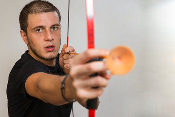 Young boy using a toy bow. The bow is red and the arrow is orange. Caucasian white man with short hair, little beard and black eyes on a white background