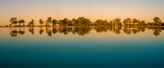 Tranquil water reflections of the cottonwood trees at Deshler Reservoir Park in Ohio - obrazy, fototapety, plakaty