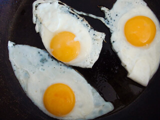3 fried eggs frying in a pan with olive oil. Three fried eggs in cast iron frying pan sprinkled with ground black.