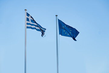 Greek and European Flag waving on two parallel flagpoles next to each other in front of a clear...
