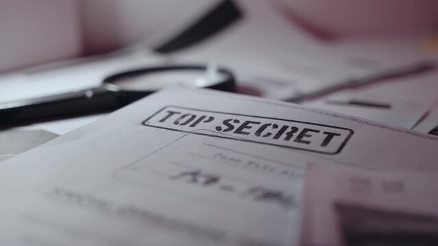 Close up on Top Secret document text with stamp with classified information. Camera moves around paper with rubber stamp of secret sensitive content. Magnifying glass next to it laid on office desk