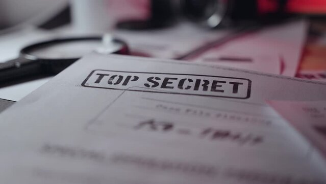 Close up top secret stamped document with magnifying glass next to it on desk. Leaked sensitive paper in dark room or military or government agency or spy network. Classified information in text