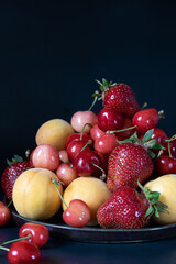 Strawberries, apricots and cherries on a round platter. Close-up. Dark key.