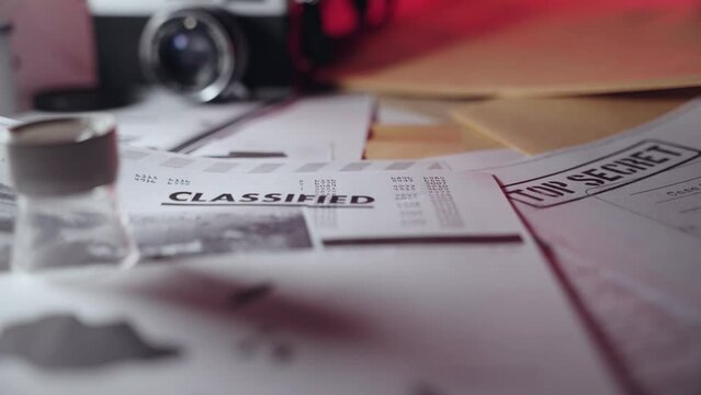 Classified document sitting on desk in dark room next to camera and folders. Confidential top secret information or secretive papers in government agency or espionage leak to press or spy network