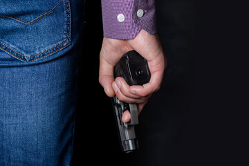 A man holding a gun in his hand behind his back, close-up view. Concepts: crime, attempted murder,...