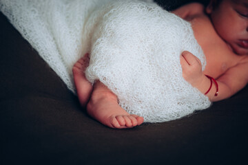Fototapeta premium Legs of a newborn. Baby feet covered with white blanket. The tiny foot of a newborn in soft selective focus. High quality photo