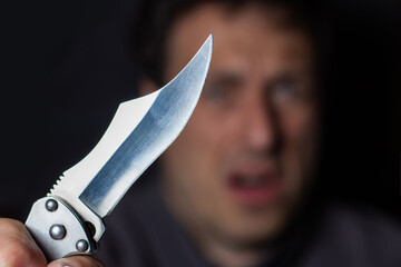 Close up of Hand with knife following young terrified man Bandit is holding a knife in hand. Threat...