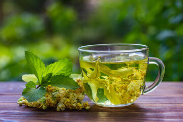 Cup with linden tea and flowers on wooden table in garden
