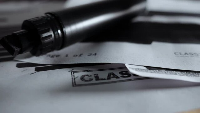 Slow move to show classified secret document with black lines and redactions. Censored text and information of government paper or memo sitting along side a black marker pen on office desk