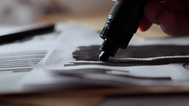Close up on black marker drawing black line on censored document on desk. Slow move as hand using pen to redact hide and erase sensitive secret information in a classified top secret memo or paper