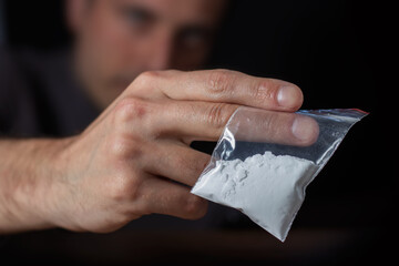 Concept drug addiction. Man hand holds plastic packet or bag with cocaine or another drugs