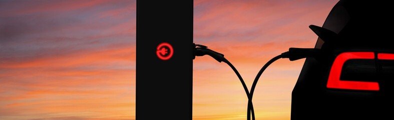 Silhouettes of electric car and charging station on a background of sunset sky