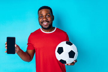 latin hispanic man with phone and football ball in studio blue background