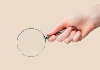 Magnifying glass lens magnifier in female hand closeup over natural beige background.