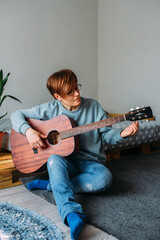  Woman with short hair enjoys playing guitar at home. Music lessons for adults