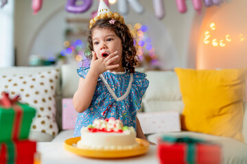 Birthday. Joyful, anniversary dressed kid daughter in party hat enjoys finger tasty sweet cake for...