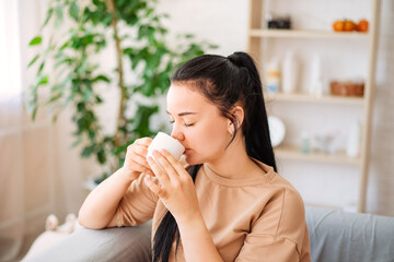 A happy young woman drinks a cup of tea on an autumn morning. A dreamy girl is sitting in the living room with a cup of hot coffee. A beautiful woman at home.