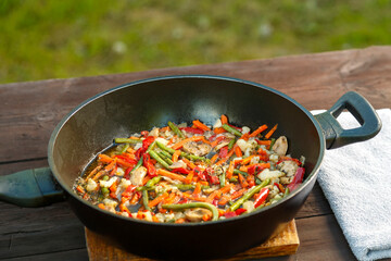 Frying pan with stewed vegetables on a napkin on a wooden table.
