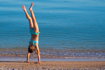 A child on the beach does sports and performs gymnastic exercises against the background of the...