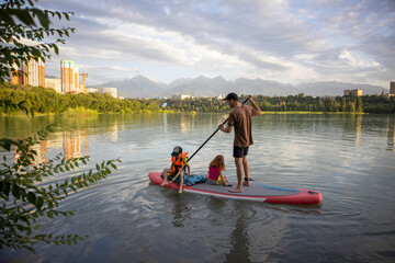 dad rides the kids on a sap board. children in life jackets.active sports life. water sports